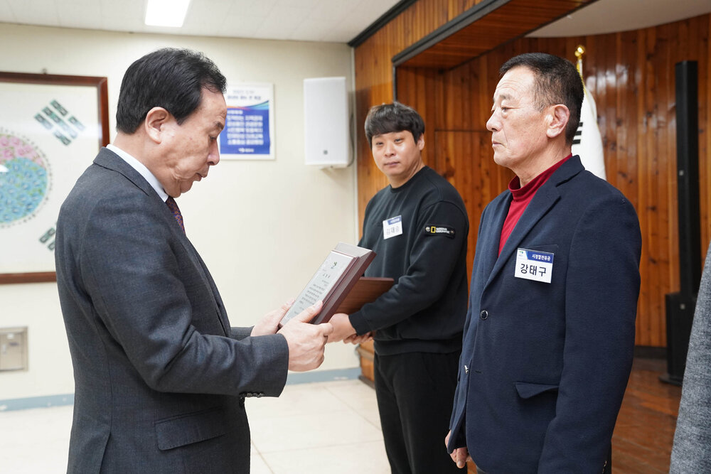 3월 정례조회에서 정장입은 남성이 남색 자켓을 입은 남성에게 패를 건내고 있다.