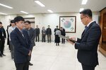 2026년 상반기 4급이하 정기인사로 정장을 입은 남성이 실내 행사장에서 한 남성에게 상장을 전달하며 내용을 읽고 있고, 남성은 남색 체크무늬 정장 자켓을 입고 두 손을 모은 상태로 서 있으며 뒤쪽으로 참석자들이 줄지어 서서 행사를 지켜보고 있다.