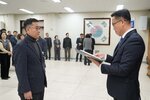2026년 상반기 4급이하 정기인사로 정장을 입고 안경을 쓴 남성이 실내 행사장에서 한 남성에게 상장을 전달하며 내용을 읽고 있고, 남성은 안경을 쓰고 짙은 색 자켓을 입은 채 서 있으며 뒤쪽에는 여러 사람들이 줄지어 서서 행사를 지켜보고 있다.